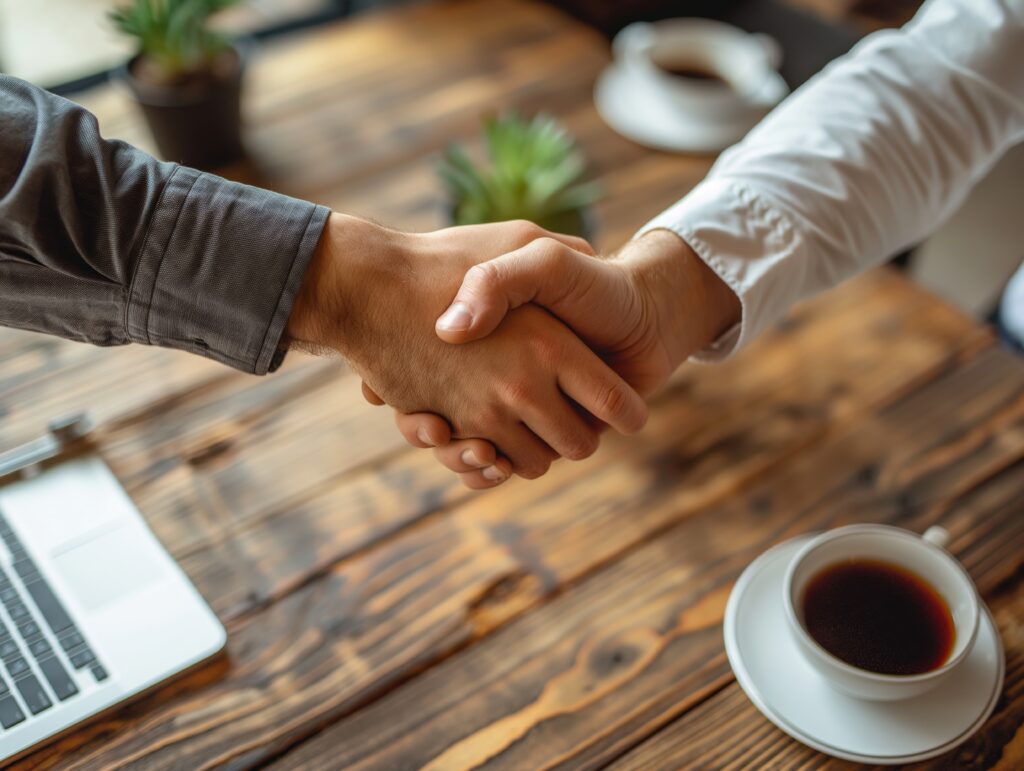 Two men sitting at a table shaking hands. Shaking hands finishing up a meeting